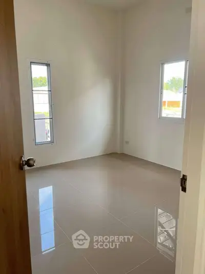 Spacious empty room with glossy tiled floor and large windows, perfect for customization.