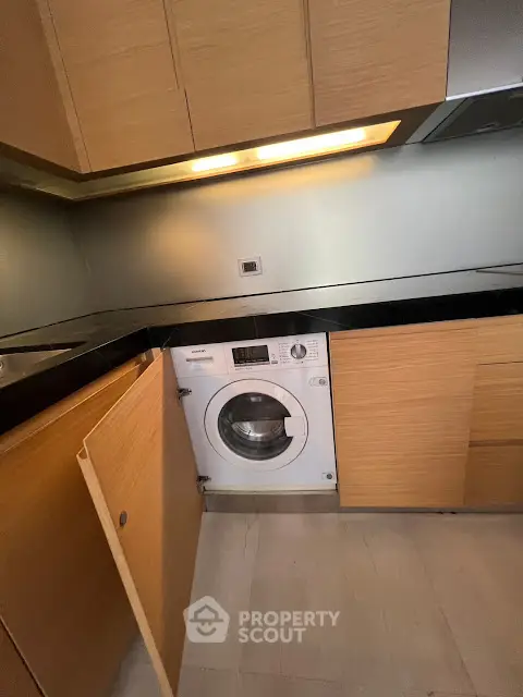 Modern kitchen with integrated washing machine and sleek wooden cabinetry.
