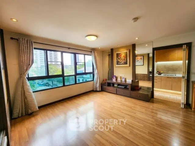 Spacious living room with wooden flooring and large windows offering city views.