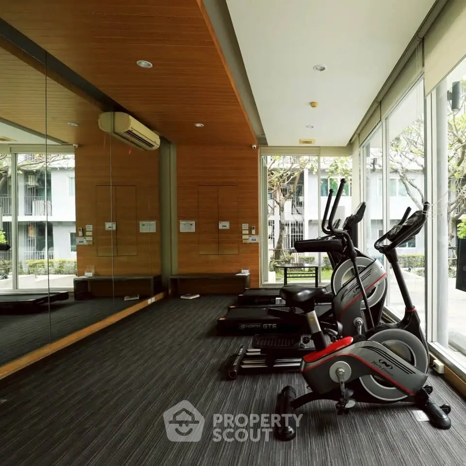 Modern gym with exercise equipment and large windows in a residential building.