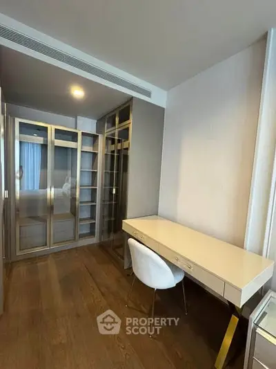 Modern study room with sleek desk and glass-door storage in a stylish apartment.