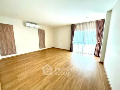 Spacious empty room with wooden flooring and large window with curtains