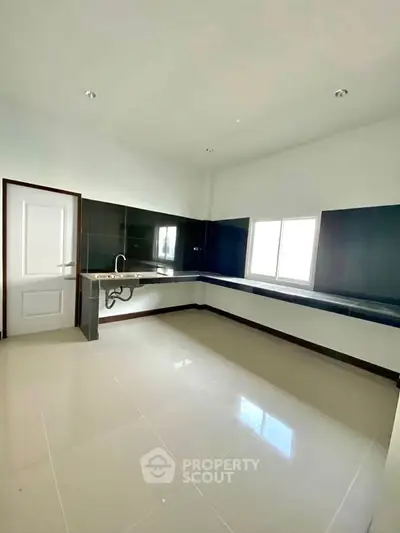 Spacious modern kitchen with sleek black and white design, featuring ample counter space and natural light.