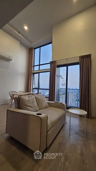 Spacious living room with high ceilings and city view, featuring modern furniture and large windows.