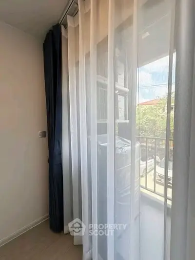 Bright room with sheer curtains and view of balcony and greenery.