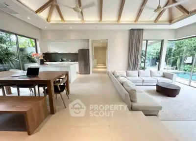 Spacious open-plan living room with modern kitchen and pool view, featuring high ceilings and elegant decor.