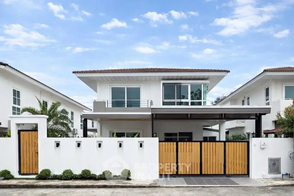 Modern two-story house with sleek design and wooden gate under a clear blue sky.