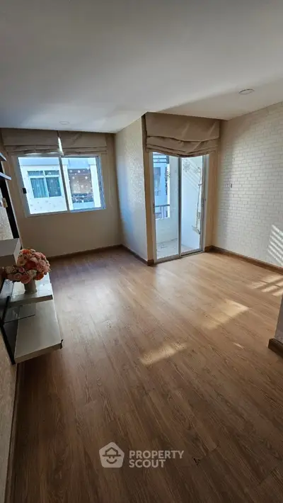 Spacious sunlit room with wooden flooring and large windows, perfect for a cozy living area.