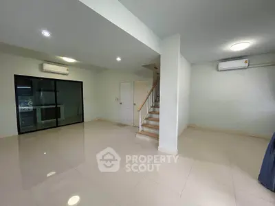 Spacious modern living room with sleek tile flooring and staircase, featuring air conditioning and ample natural light.