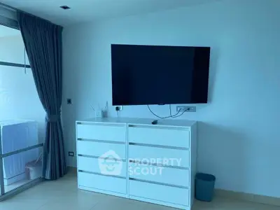 Modern living room with sleek white furniture and wall-mounted TV, featuring a large window with curtains.