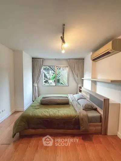 Cozy bedroom with large window and modern air conditioning unit, featuring elegant wooden flooring and stylish decor.