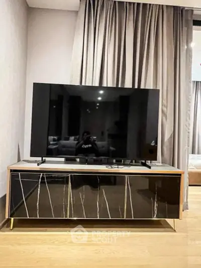 Modern living room with sleek TV stand and large flat-screen TV, elegant curtains, and stylish decor.