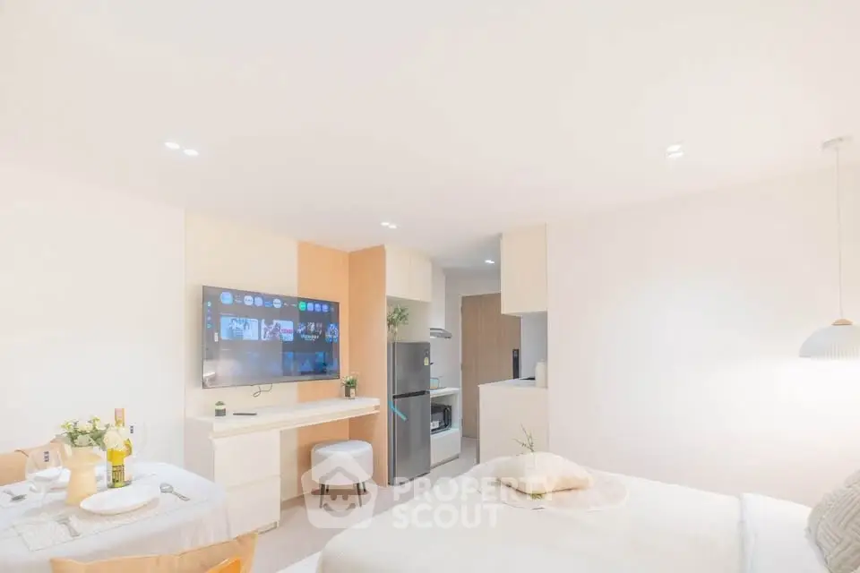 Modern studio apartment with open layout, featuring a cozy bed, wall-mounted TV, and sleek kitchen area.