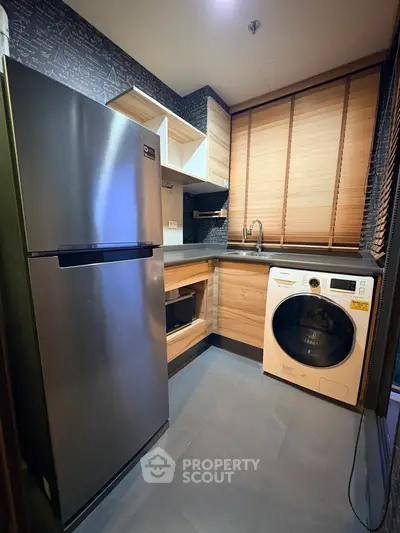 Modern kitchen with stainless steel fridge and washing machine, sleek wooden cabinets, and stylish blinds.