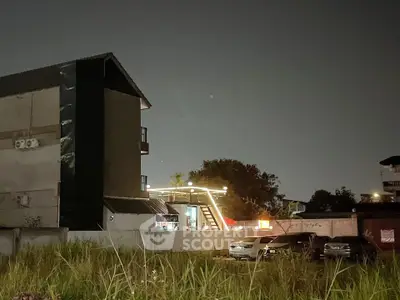 Night view of a modern building with parking area and illuminated rooftop terrace.
