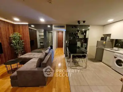 Modern open-plan living room with sleek kitchen and cozy seating area, featuring stylish lighting and wooden flooring.