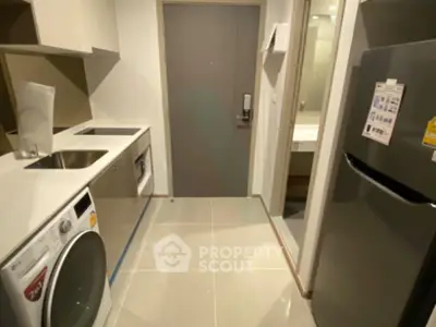 Modern apartment entryway with sleek kitchen appliances and washing machine.