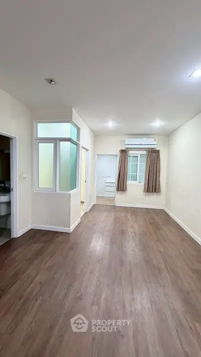 Spacious empty room with wooden flooring and large window, ideal for customization.