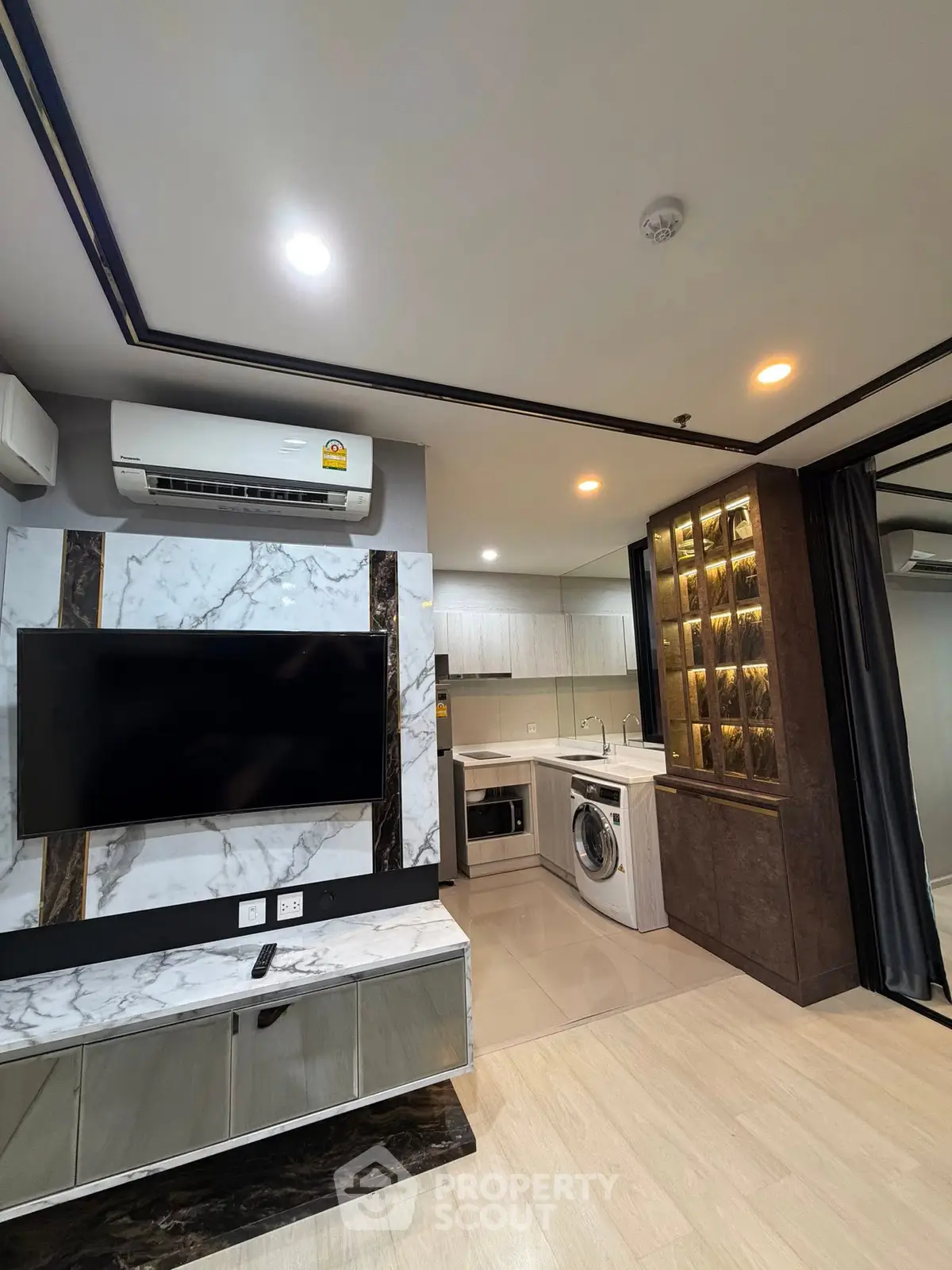 Modern living room with marble TV wall and open kitchen featuring washing machine and sleek cabinetry.