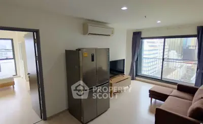 Modern living room with city view, featuring a cozy sofa, flat-screen TV, and stainless steel refrigerator.