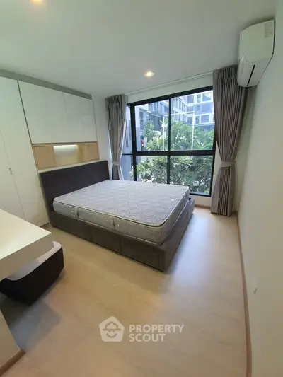 Modern bedroom with large window and built-in storage in a stylish apartment.