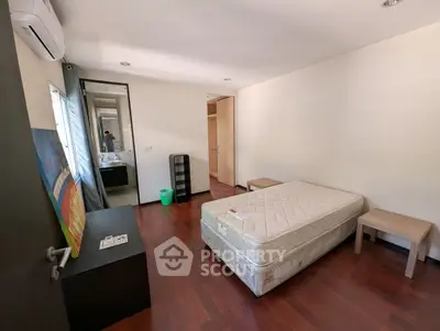 Spacious bedroom with hardwood floors and modern furnishings in a well-lit apartment.
