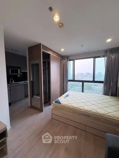 Modern bedroom with large window and city view, adjacent to a compact kitchen area.