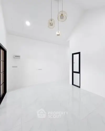 Minimalist white room with high ceiling and modern pendant lights.