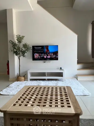 Modern living room with stylish decor and wall-mounted TV under staircase.