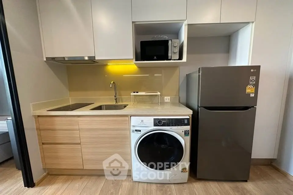 Modern kitchen with sleek appliances and wooden cabinetry, featuring a washing machine and fridge.