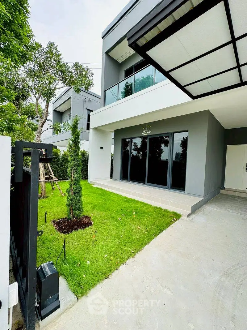 Modern two-story house with sleek design and lush green lawn, featuring large glass doors and a spacious driveway.