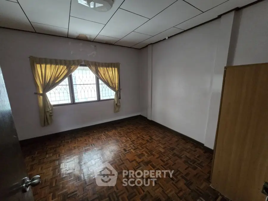 Spacious empty room with parquet flooring and window curtains