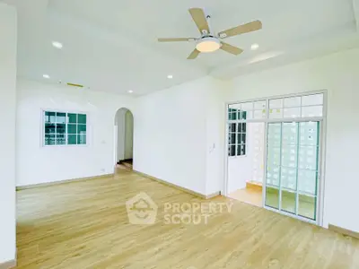 Spacious modern living room with wooden flooring and ceiling fan, featuring large windows for natural light.