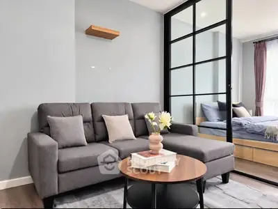 Modern living room with stylish gray sofa and glass partition leading to bedroom