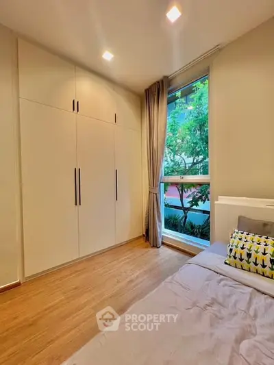 Cozy bedroom with large window and built-in wardrobe, offering a serene view of lush greenery.