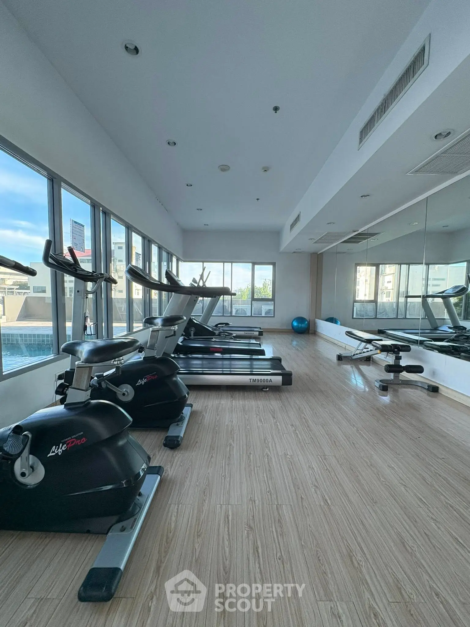 Spacious gym with modern equipment and large windows offering city views.