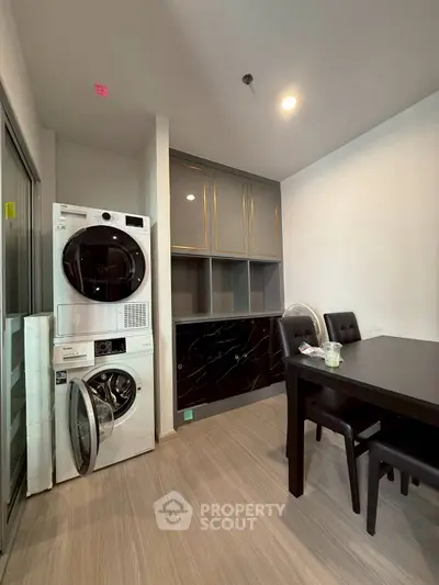 Modern dining area with sleek black table and chairs, featuring a stacked washer and dryer unit.