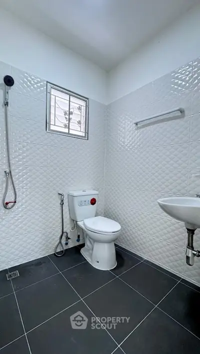 Modern bathroom with sleek white tiles and black flooring, featuring a toilet and shower area.