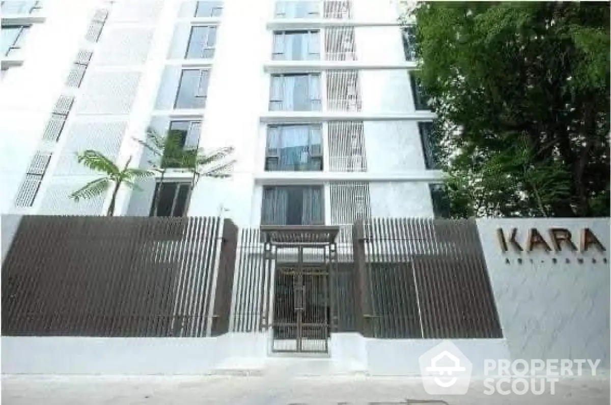 Modern apartment building with sleek design and gated entrance in lush surroundings.