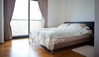 Spacious bedroom with large window and elegant curtains, featuring a cozy bed and wooden flooring.