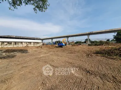 Vacant land with construction equipment near elevated railway, ideal for development opportunities.