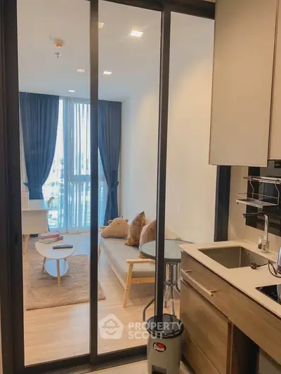 Modern living room with open kitchen, featuring sleek design and large windows for natural light.