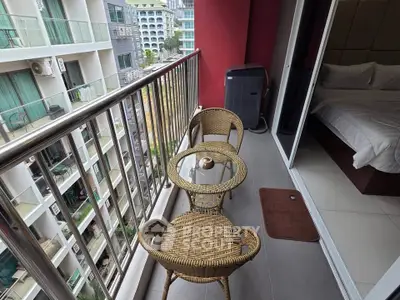 Charming balcony with wicker furniture and city view, adjacent to a cozy bedroom in a modern apartment.