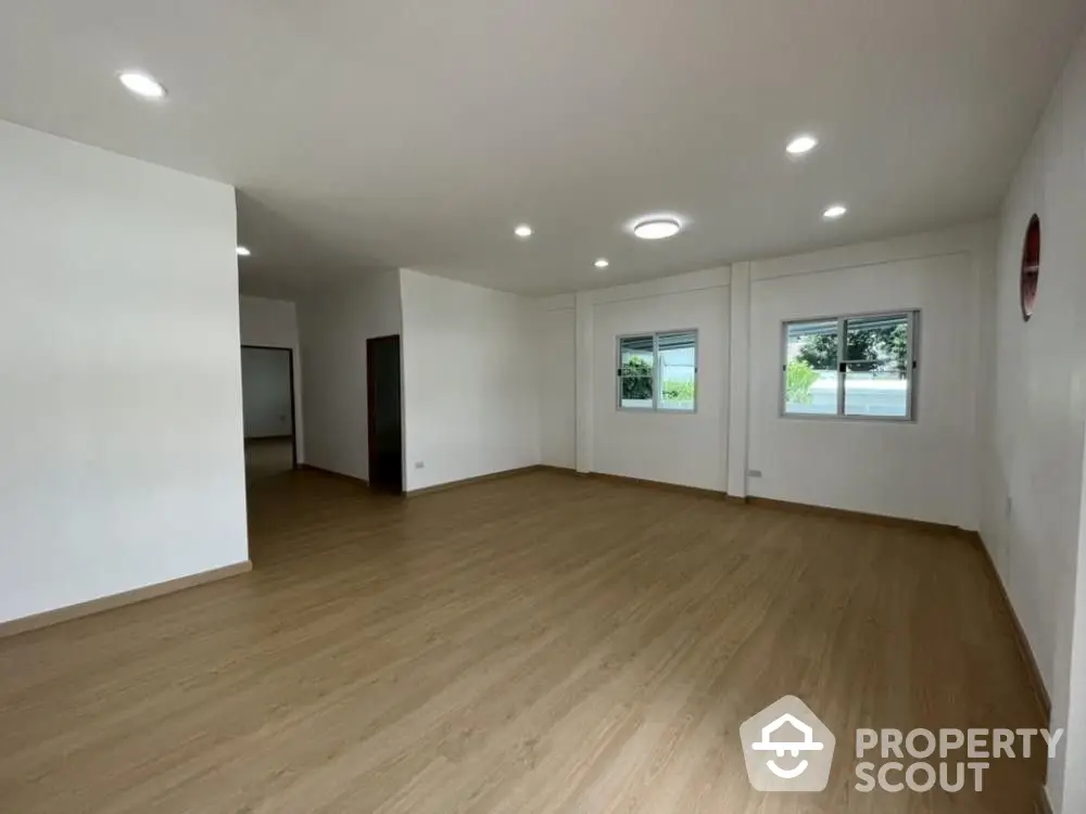 Spacious and well-lit living room with modern laminate flooring and ample natural light from large windows, perfect for family gatherings.