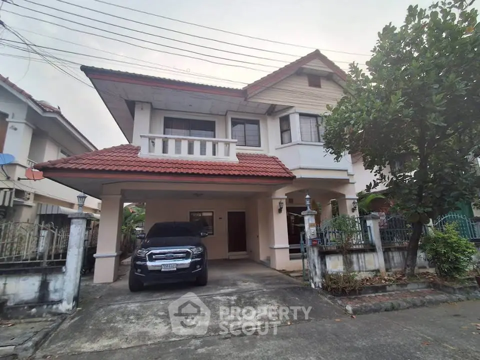 Charming two-story house with driveway and car, featuring a red-tiled roof and lush greenery.