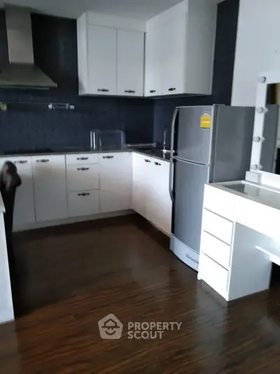 Modern kitchen with sleek cabinets and stainless steel fridge in a cozy apartment.