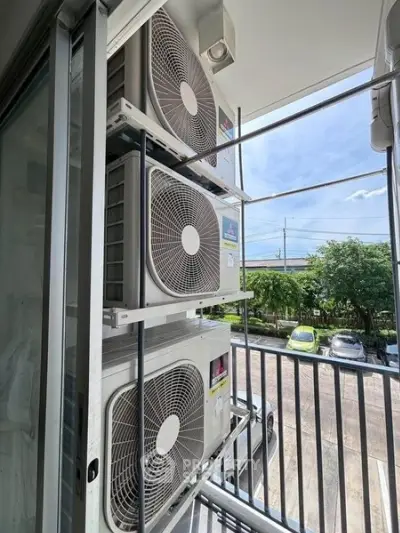 Outdoor view of air conditioning units on a balcony with street and greenery in the background.