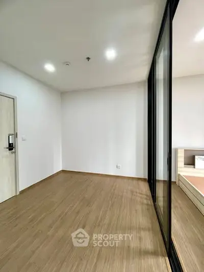 Spacious modern bedroom with wooden flooring and large glass sliding doors.