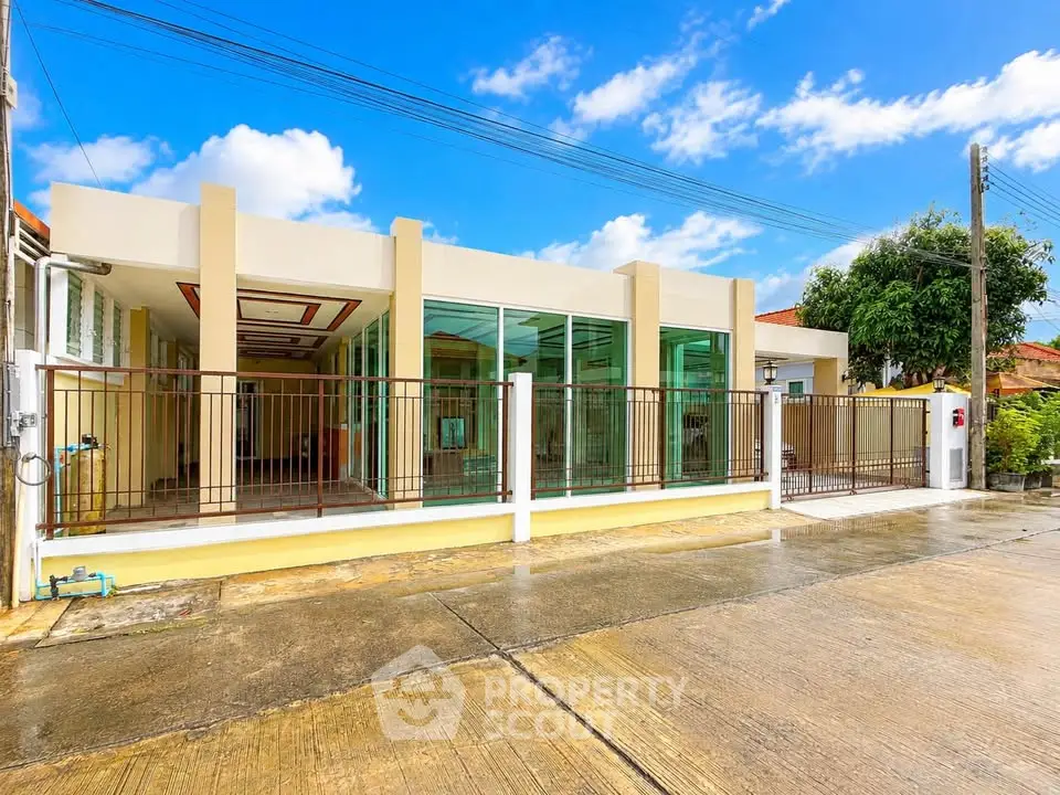 Modern single-story house with large glass windows and gated entrance in a sunny neighborhood.