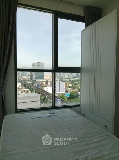 Modern bedroom with city view from large window, featuring a sleek wardrobe and comfortable bed.